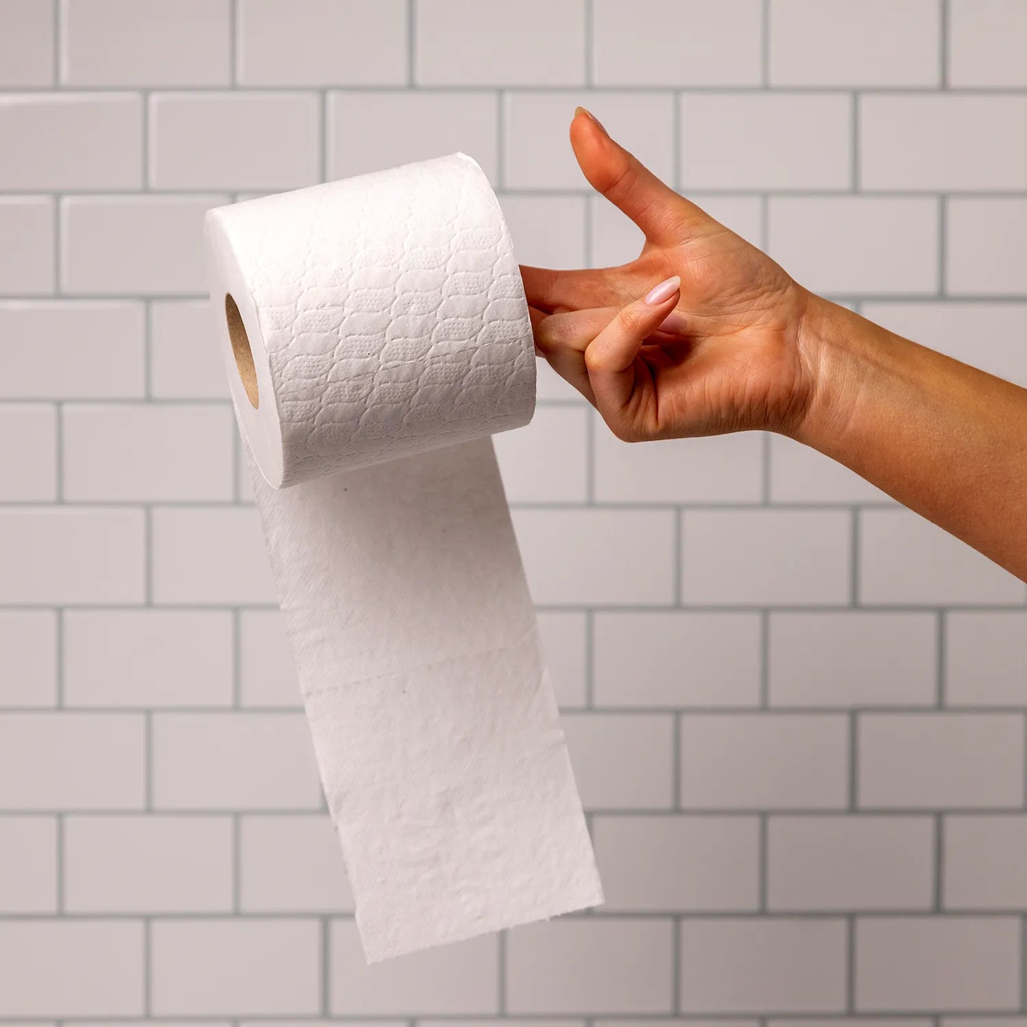 White toilet paper held by a woman using two fingers in front of a white tiled background