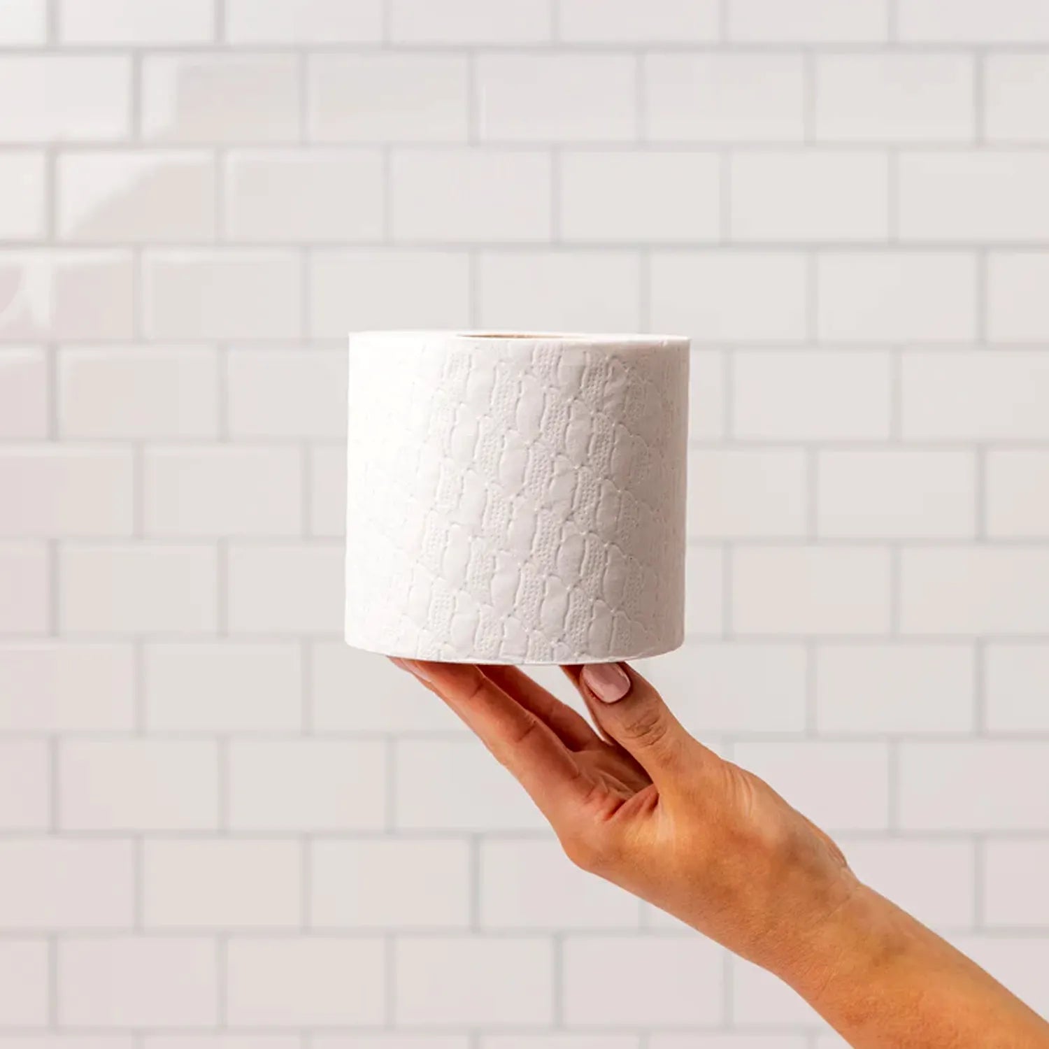 White recycled toilet paper being held by a woman in front of a white tiled wall