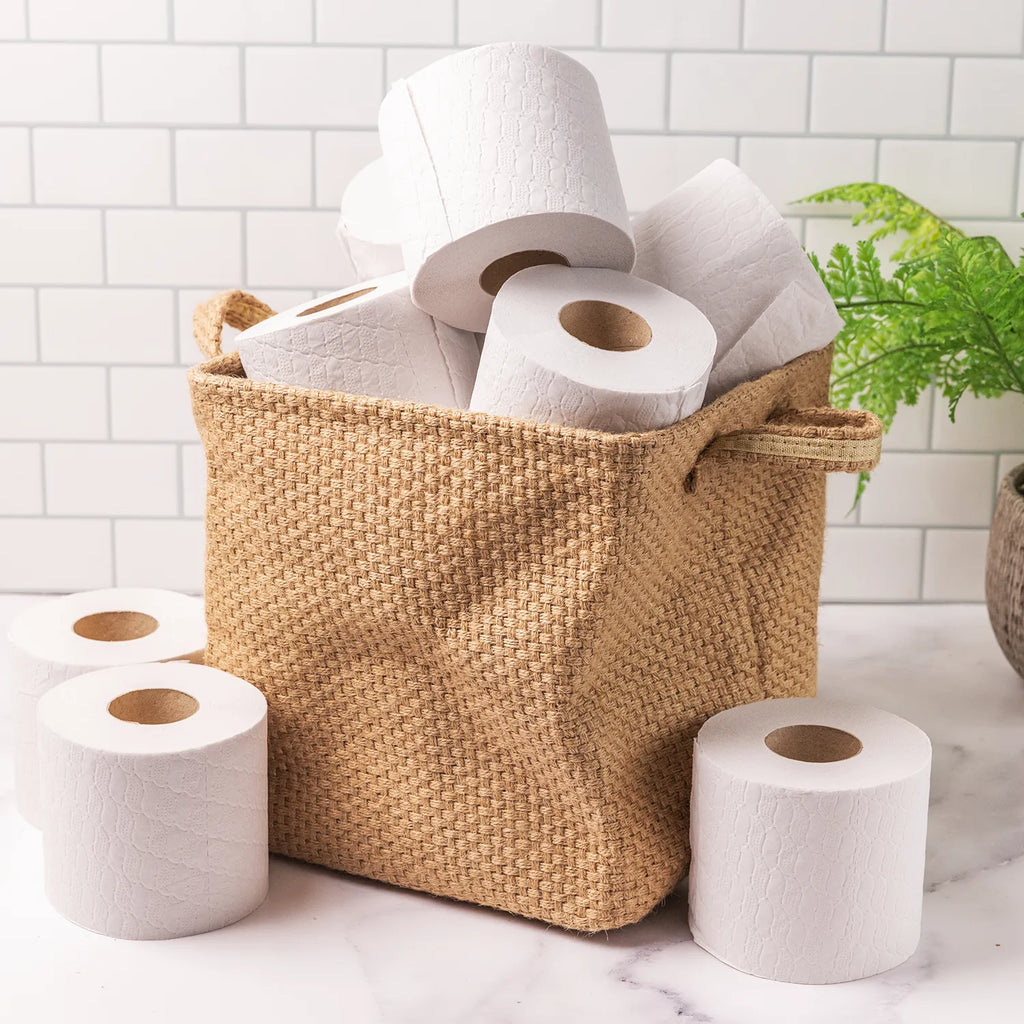 Basket full of white toilet paper in a white tiled bathroom with plant